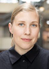 En kvinna i blont uppsatt hår och svart skjorta