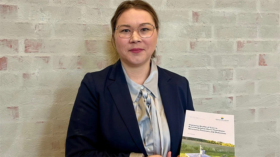 En mörkhårig kvinna med glasögon och mörkblå kavaj håller upp en bok.