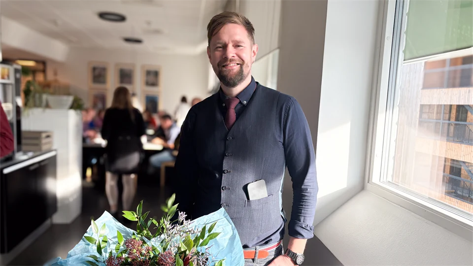 En man med kort brunt hår ler med blommor framför sig