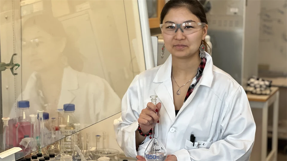 En kvinna i vit rock och skyddsglasögon står i ett laboratorium.