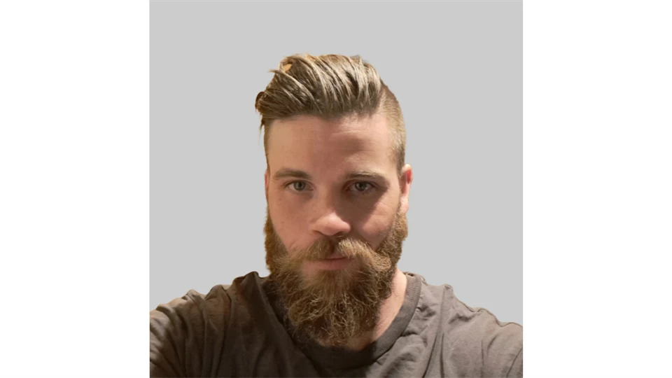 Man i ljusbrunt hår, skägg och brun tröja. 