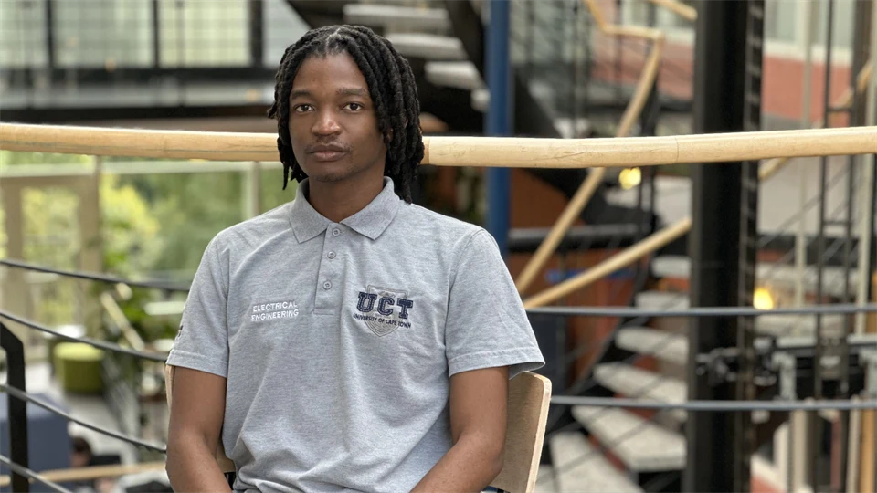 En man med svart hår sitter på en stol framför en trappa