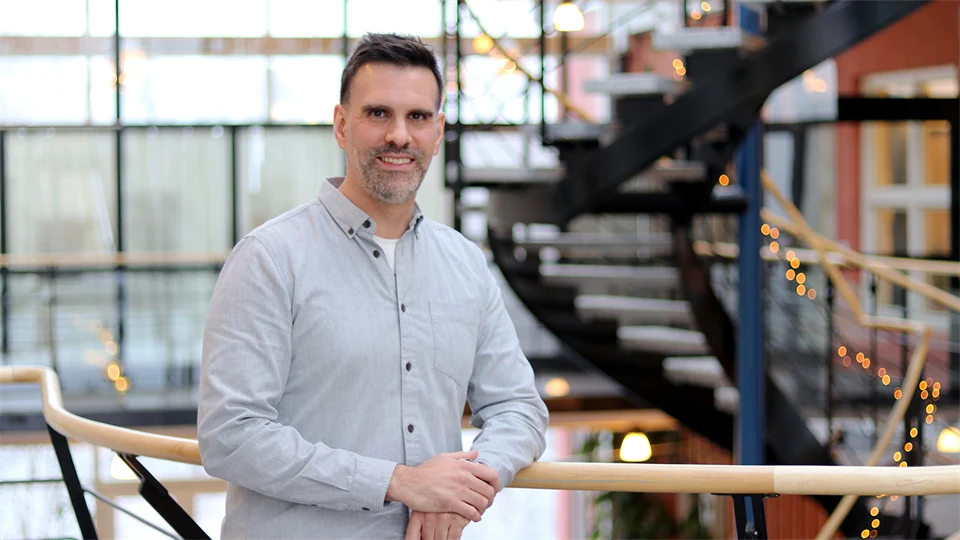 En man i ljus skjorta står vid ett staket och ler in mot kameran. 