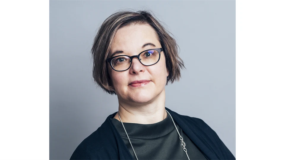 A woman with dark hair, glasses, wearing a black top.