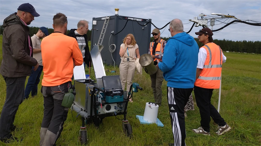 Several people are standing on a grassy field and looking at measuring equipment.