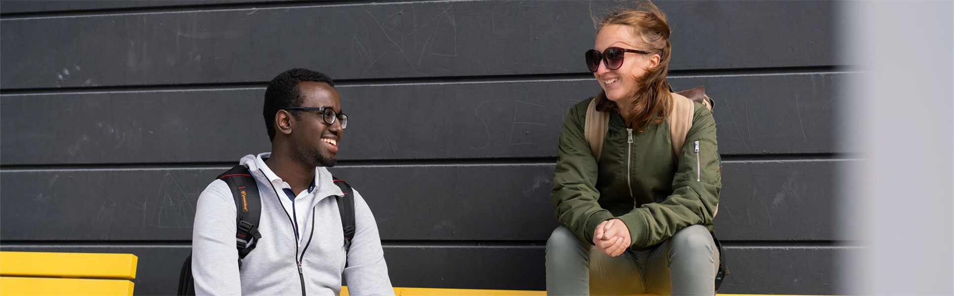 Två studenter som sitter på gul bänk. 