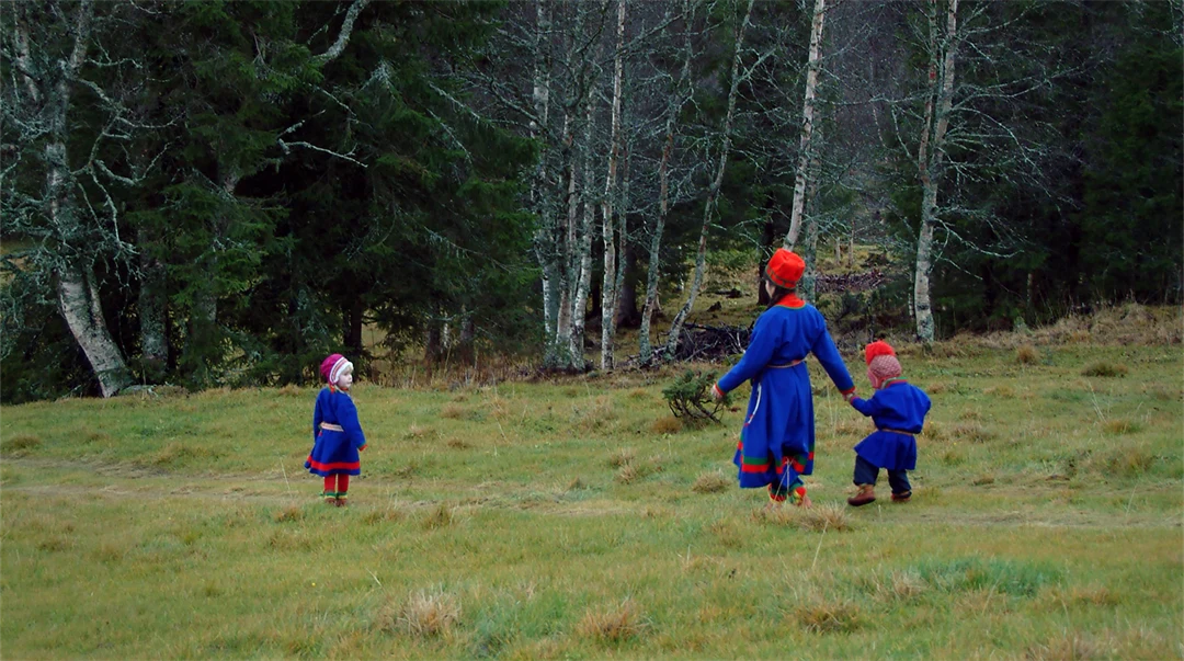 Kvinna och två barn i sydsamiska dräkter går över ett fält.