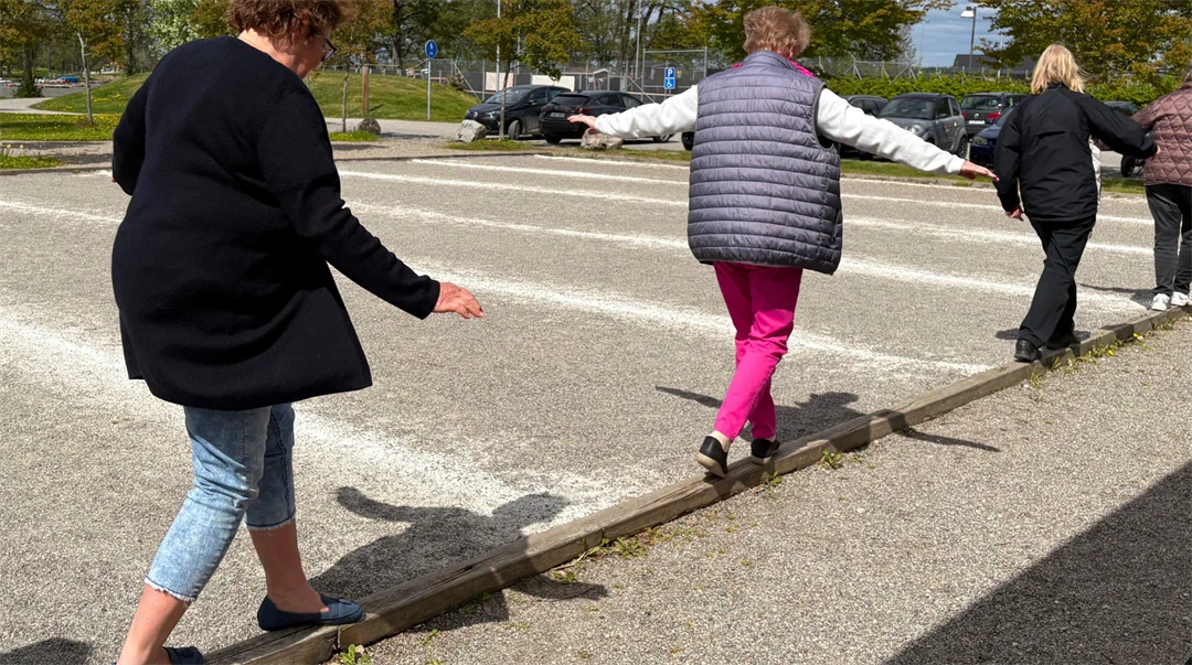 Kvinnor balanserar på en smal bräda vid en grusplan