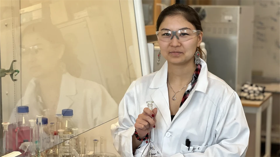 En kvinna i vit rock och skyddsglasögon står i ett laboratorium.