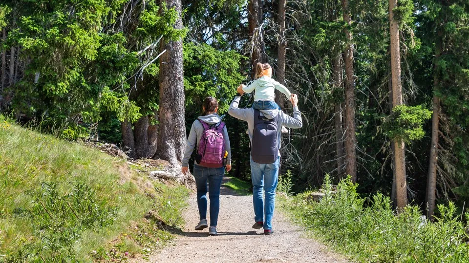 kvinna med ryggsäck  och man med barn på axlarna vandrar i skogen