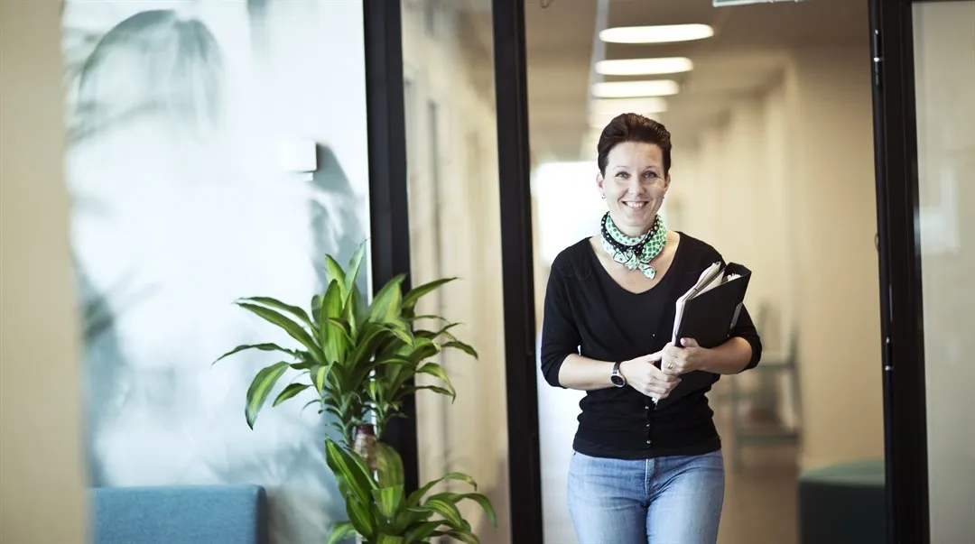 En tjej som står i en korridor med en stor palm i bakgrunden.