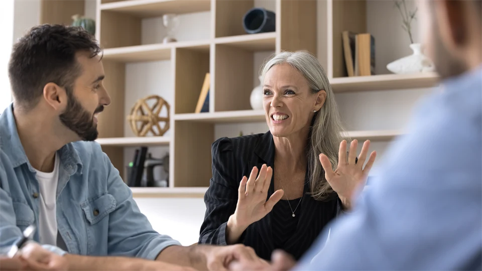 Cheerful senior business leader woman talking to team of younger employees, speaking with toothy smile, telling creative idea for brainstorming, enjoying corporate communication. Banner shot