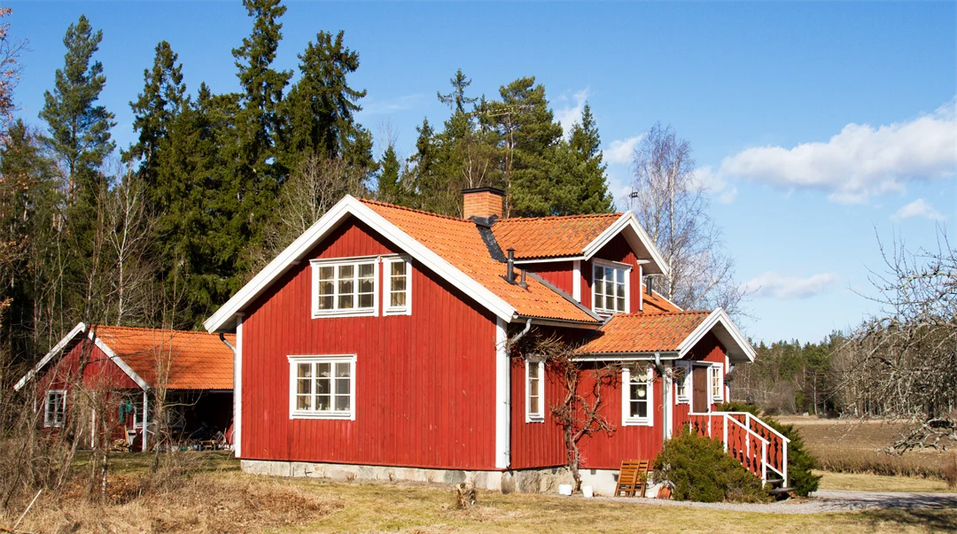 Rött hus med vita knutar vid skogsbrynet.