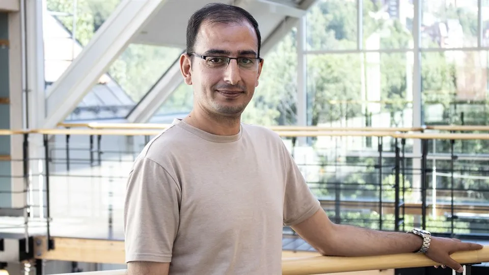 A man with glasses and dark hair is posing in front of the camera.