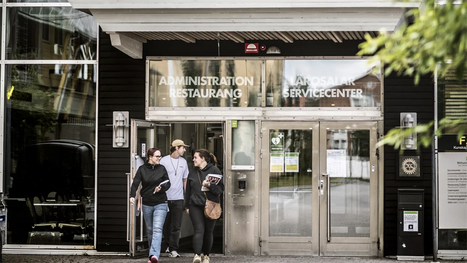 Glasdörrar på en byggnad. Tre människor går ut.