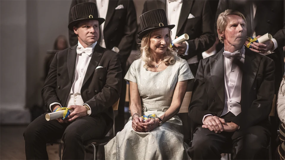 Finklädda personer med lagerkransar och doktorshattar på en scen.