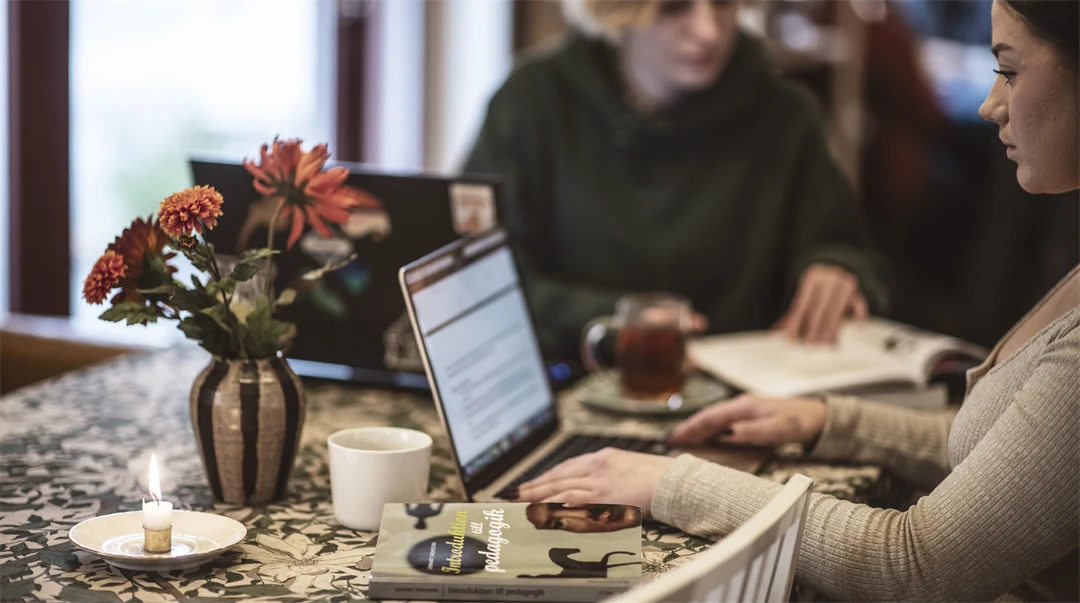Två kvinnor sitter vid ett bord, tittar på en dator.