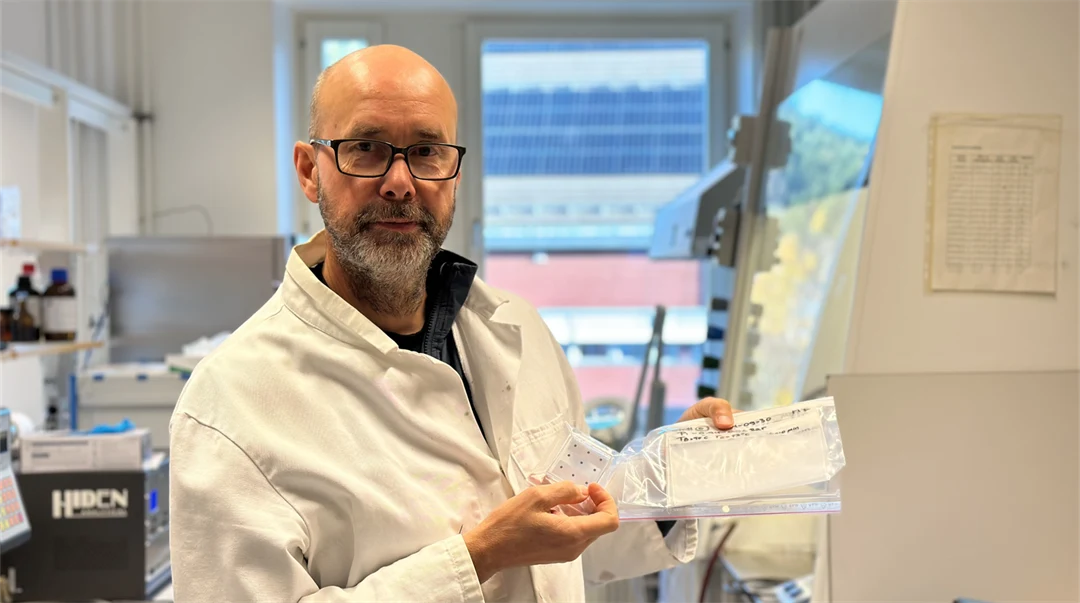 Man med skägg och glasögon i labbrock.