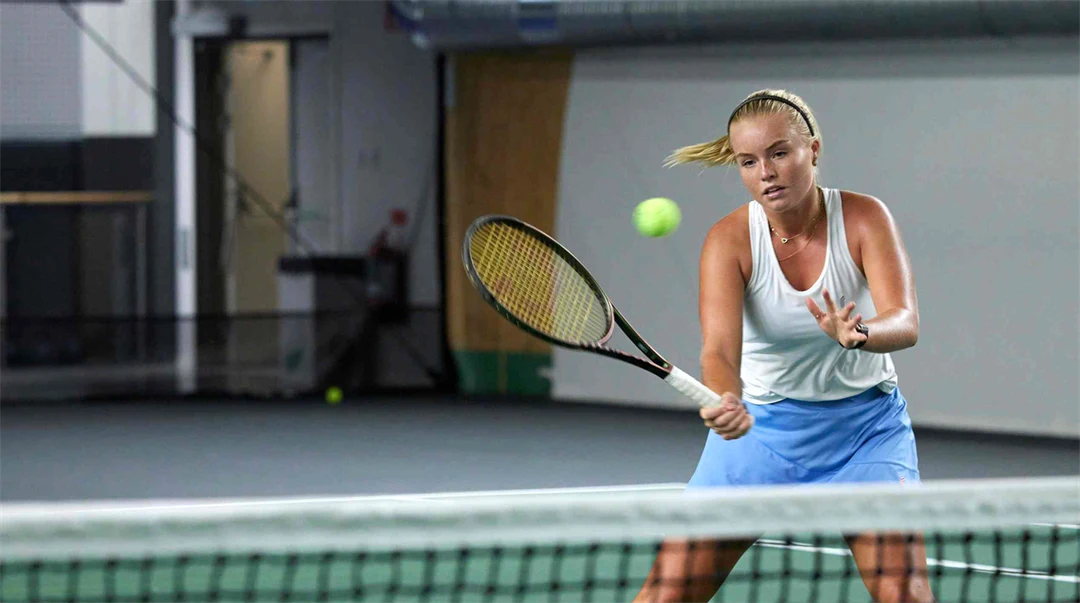 Kvinna som spelar tennis inomhus, hon står vid nät och ska till att slå en volley.