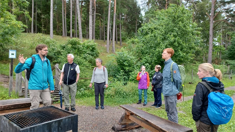 En grupp människor står och pratar vid en eldplats i stadsnära landskap