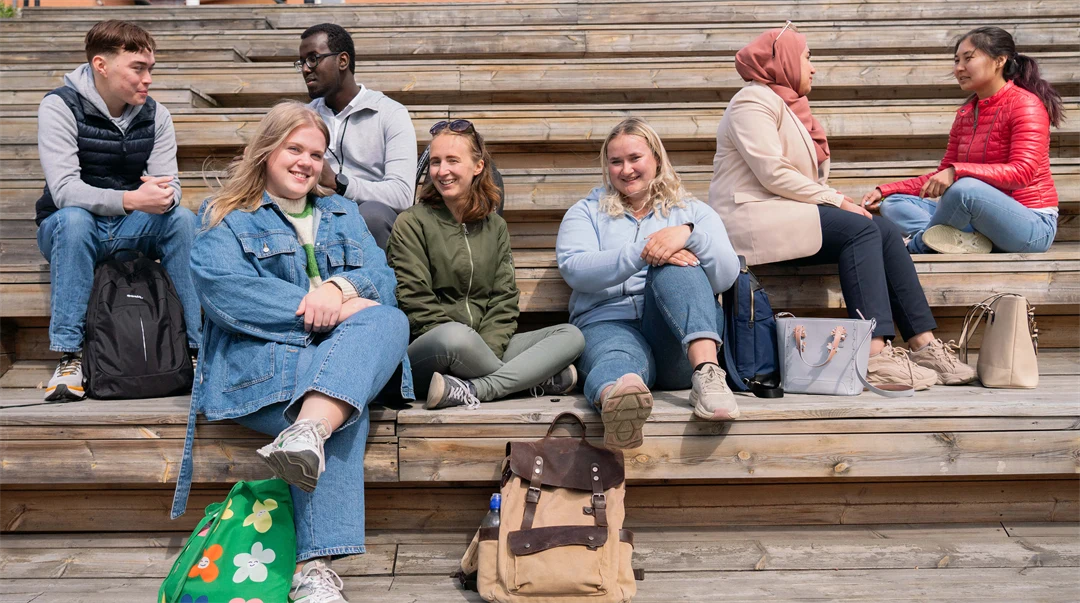 A group of students sit on a wooden staircase and talk.