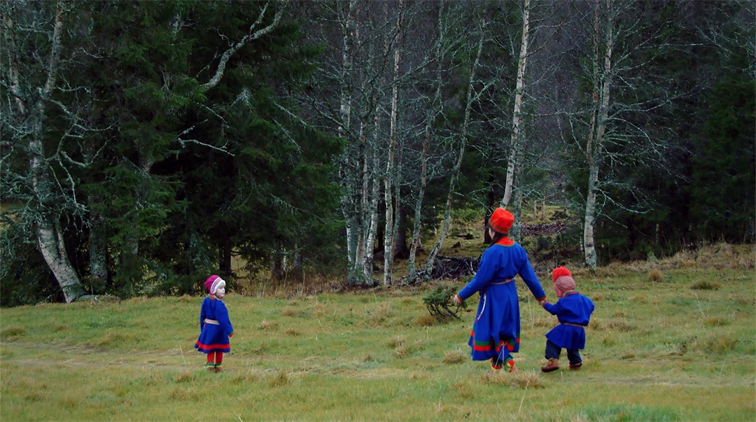Kvinna och två barn i sydsamiska dräkter går över ett fält.