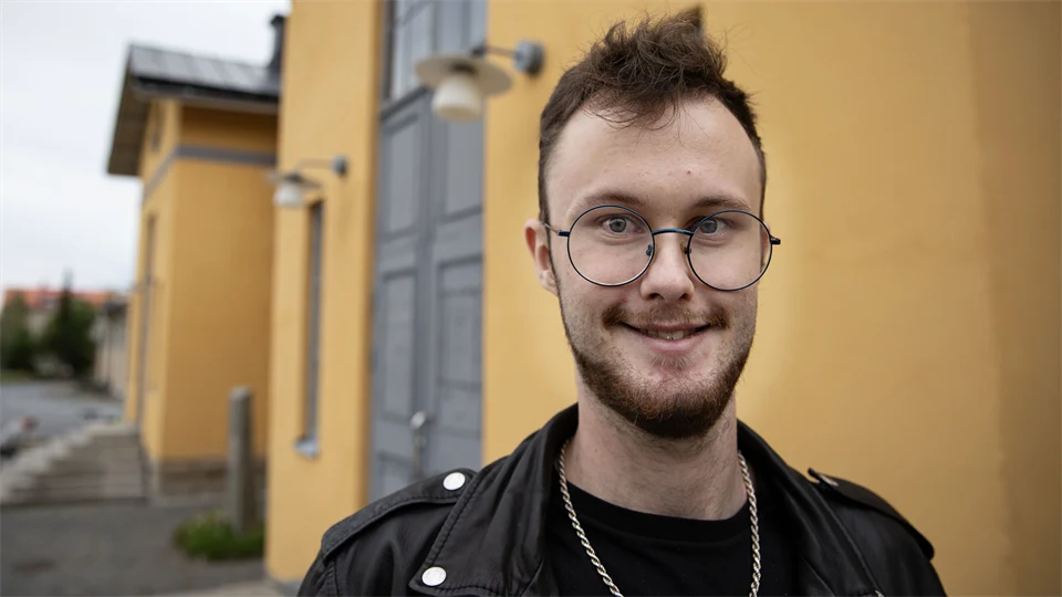 Man med runda glasögon och skinnjacka står utanför en gul byggnad.