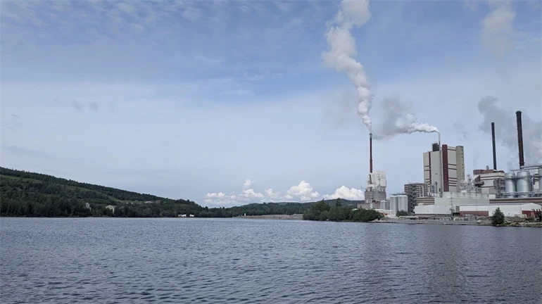 Fabrik med bolmande rök invid vatten