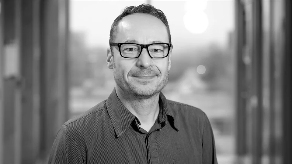 En bild i svartvitt på en man som tittar in i kameran.