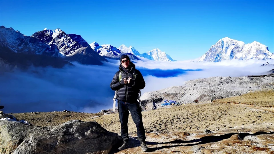 En man står på en slätt med höga bergstoppar i bakgrunden.