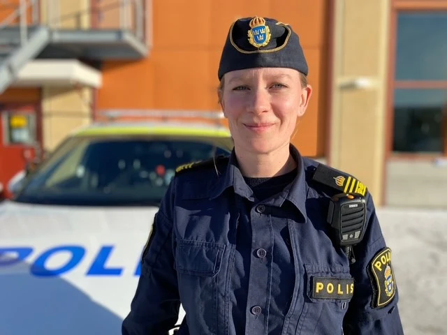 Kvinna i polisuniform står framför en polisbil
