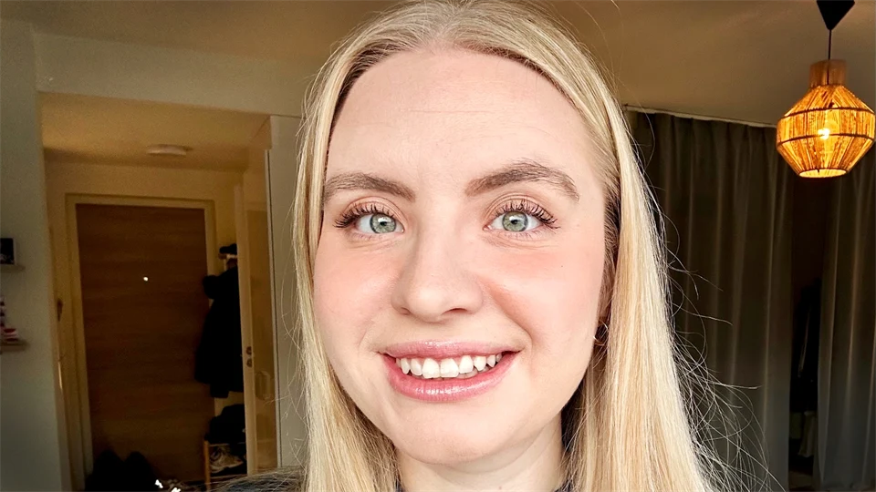 Kvinna med långt blont hår ler in i kameran.