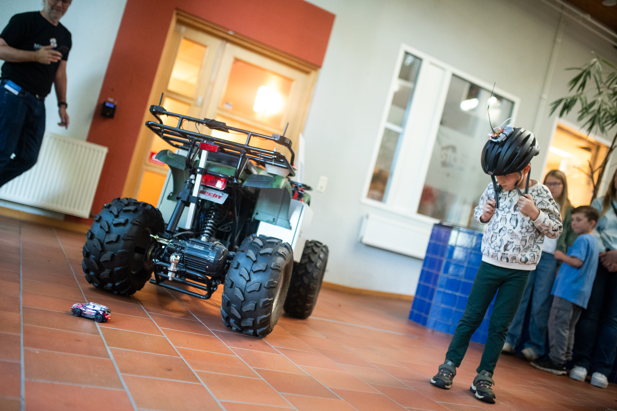 An ATV and a toy car and a kid with a bike helmet on. 
