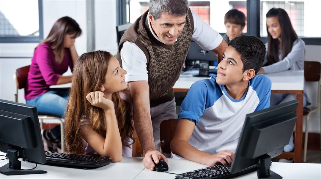 Manlig lärare använder dator medan elever tittar på honom i klassrummet