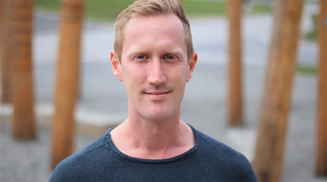 A man with dark blue sweater, wooden logs visible in the background