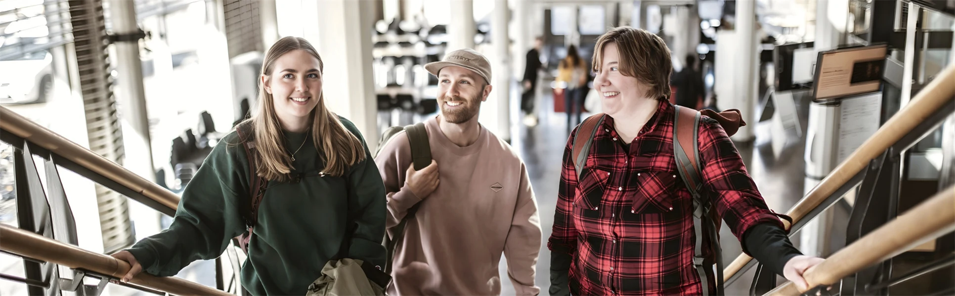 Tre unga studenter står i en trappa. De är alla glada. 