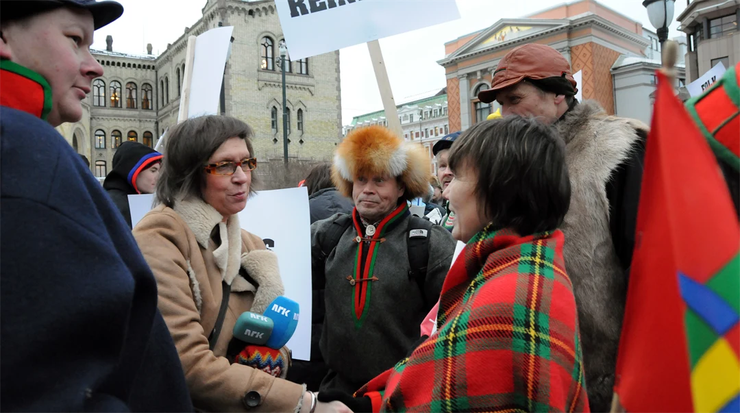 Två kvinnor skakar hand. Någon i bakgrunden håller upp ett plakat.