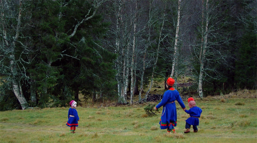 Kvinna och två barn i sydsamiska dräkter går över ett fält.