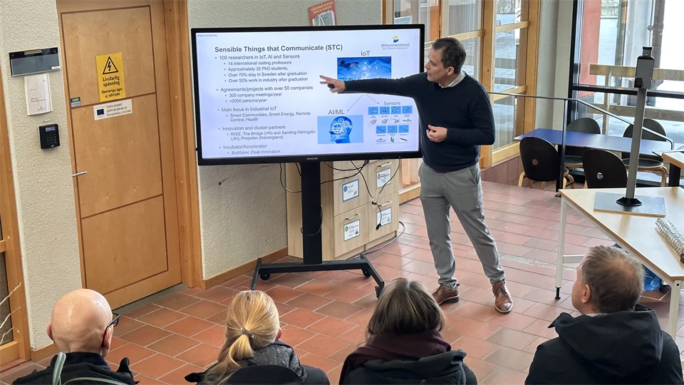 En man med svart tröja och mörkt hår står framför en tavla och pekar