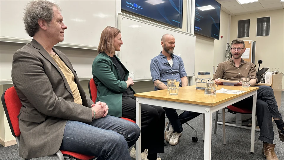 Fyra personer sitter runt ett fyrkantigt bord och samtalar