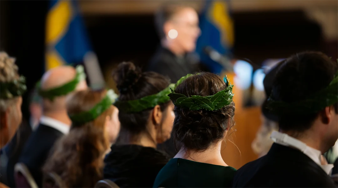 Personer som sitter i stolar och på deras huvuden bär de lagerkransar.
