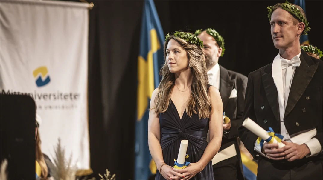 Finklädda personer med lagerkransar står på en scen med diplom i handen.