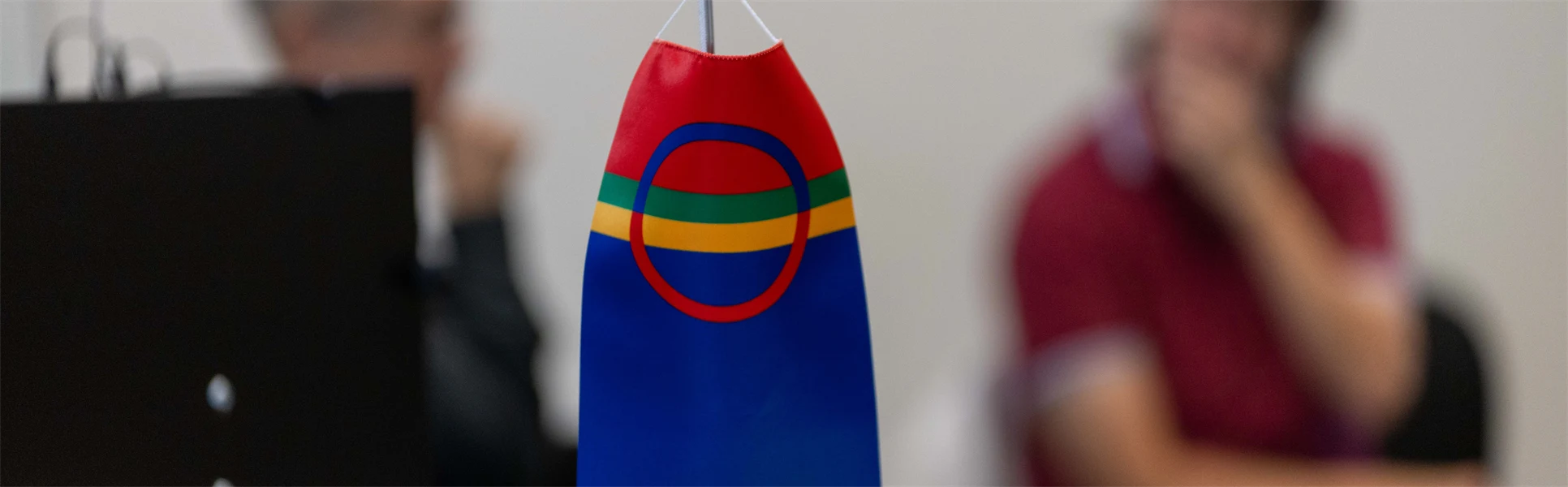 Den samiska flaggan i förgrunden och två människor utan fokus i bakgrunden