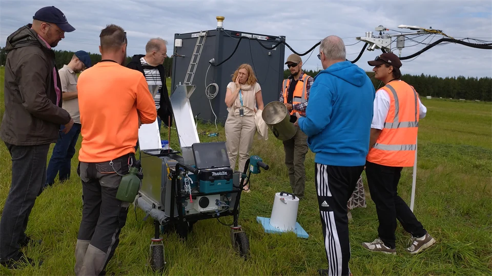 Several people are standing on a grassy field and looking at measuring equipment.