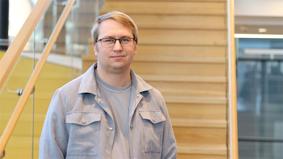 A man with glasses stands in front of a staircase.