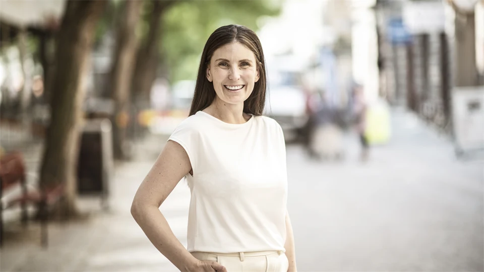 Kvinna med brunt hår, klädd i en vit topp ler mot kameran