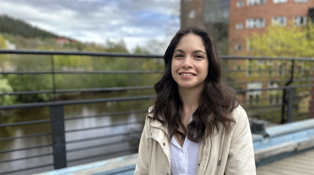 Mörkhårig kvinna med beige jacka ler mot kameran.