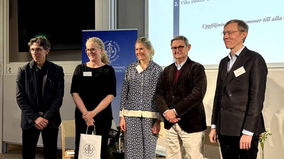 Tre män och två kvinnor på scenen i en aula.