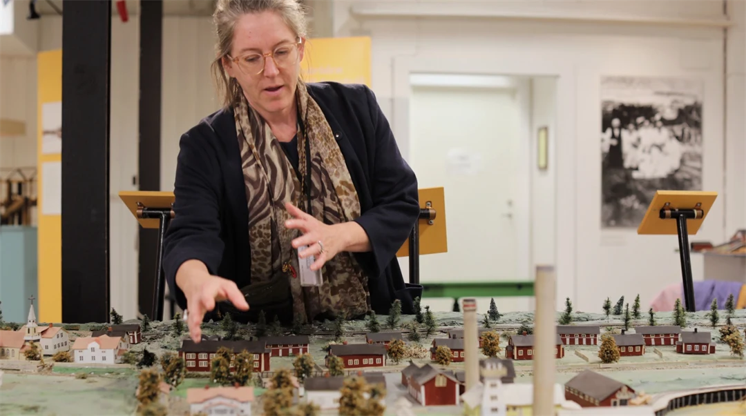 Kvinna står bredvid och visar en modell av en by i miniatyr 