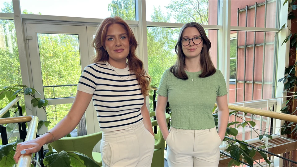 Två unga kvinnor står tillsammans i en ljusgård.